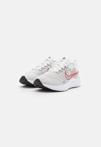 Weiße Sportschuhe mit einer strukturierten Oberseite, ausgestattet mit einem roten Swoosh, flachen Schnürsenkeln und einer Gummisohle, die für Komfort und Unterstützung ausgelegt sind.