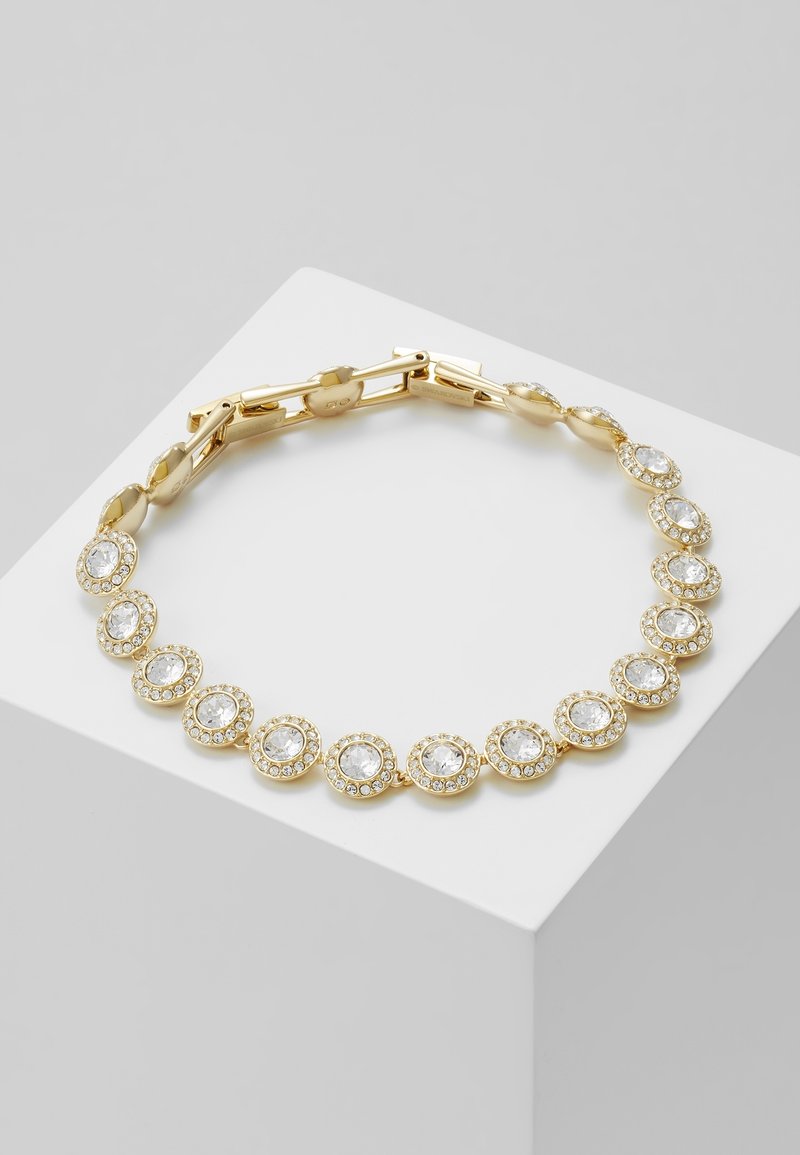 Bracelet en or avec des cristaux clairs ronds entourés de petites pierres, exposé sur une surface géométrique blanche.