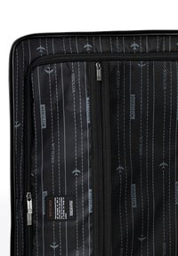 Vnitřek černé cestovní tašky s síťovou kapsou a tištěnými vzory letadel a čárkovaných čar. Obsahuje zip a značkovou etiketu.