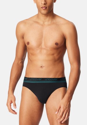 Schwarze Baumwollslips mit einem kontrastierenden türkisfarbenen Bund, der das "uncover"-Logo trägt. glatte Textur und enganliegendes Design.