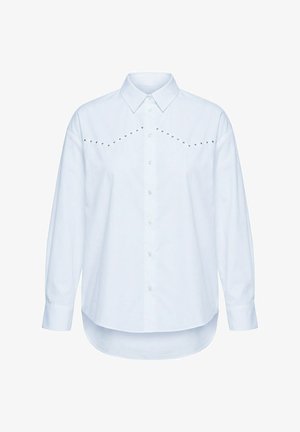 Camicia bianca a maniche lunghe con bottoni, colletto appuntito, orlo curvo e linee diagonali di piccoli borchietti metallici sul petto.