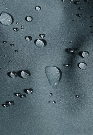 Gocce d'acqua che si raggruppano su un tessuto impermeabile liscio di colore grigio scuro, mostrando la tensione superficiale e i dettagli della trama.