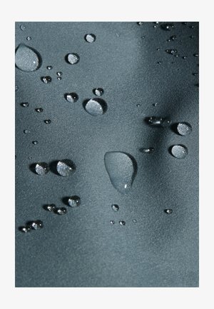 Gocce d'acqua che si raggruppano su un tessuto impermeabile liscio di colore grigio scuro, mostrando la tensione superficiale e i dettagli della trama.