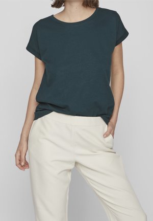 Dunkelblaues kurzärmeliges T-Shirt mit Rundhalsausschnitt, kombiniert mit cremefarbenen Hosen. Der Stoff des T-Shirts wirkt weich und glatt.