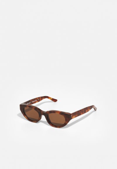 Lunettes de soleil écaille de tortue avec des verres marron ; monture rectangulaire, branches épaisses, texture lisse et légère forme en oeil de chat.