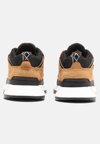 Sneakers in pelle marrone e rete nera con retro texture, suola intermedia bianca e accenti decorativi sul tallone. La vista posteriore mostra i dettagli del design.