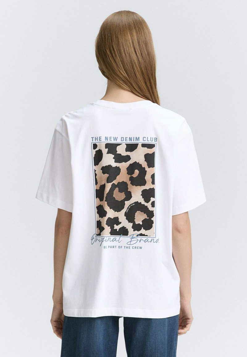T-shirt bianca in cotone con una grafica a stampa leopardata sul retro, accompagnata da testo sopra e sotto il design. Maniche corte e vestibilità rilassata.