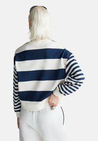 Felpa a righe blu navy e bianche con collo a giro e polsini a costine, che mostra audaci motivi a righe orizzontali e verticali.