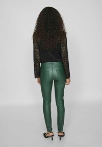 Zelene hlače iz umetnega usnja s slim fit krojem, z visokim pasom, zadnjimi žepi in v kombinaciji z dolgimi čipkastimi črnimi rokavi.