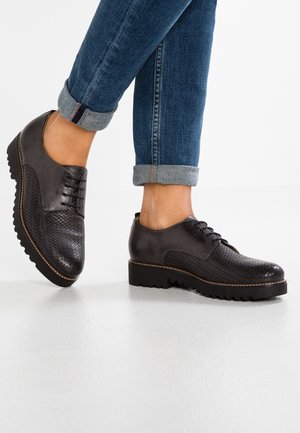 Chaussures noires en cuir avec une texture tissée et un design à lacets. Semelle épaisse et nervurée avec un détail de couture contrastant. Portées avec un jean en denim retroussé.