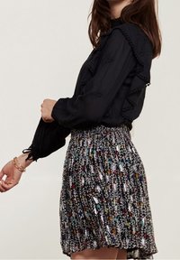 Schwarze Bluse mit Rüschendetails und dekorativen Nähten, kombiniert mit einem Rock im Blumenmuster mit mehrfarbigen Akzenten und gerafftem Bund.