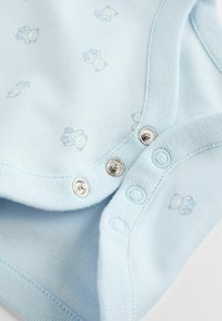 Un grenouillère pour bébé bleu clair en coton doux, ornée de petits imprimés d'ours en peluche gris et bleu, avec des fermetures à pression sur le bas.