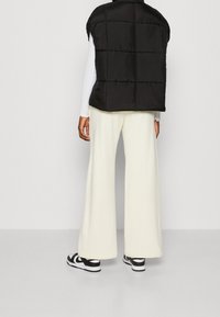 Musta puffertakki, jossa on tikattu malli, valkoisen pitkähihasen paidan päällä, yhdistettynä kermankeltaisiin leveisiin housuihin ja musta-valkoisiin tennareihin.