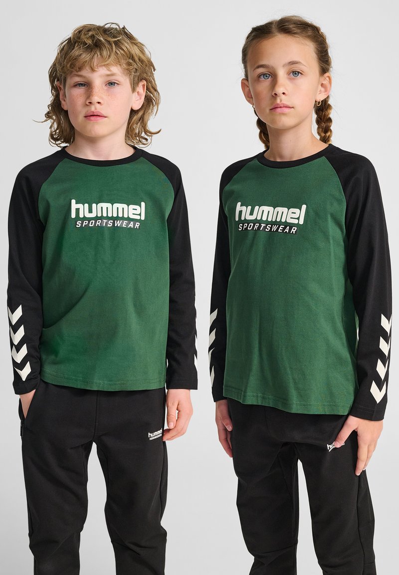 Magliette di cotone verde a maniche lunghe con maniche nere, con logo bianco e motivi a chevron. Abbinate a pantaloni neri, anch'essi con logo.