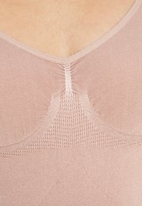 Light pink tank top featuring a V-neck, textured mesh accents, and smooth fabric with seams running down the front for added detail.