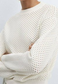 White knit sweater with open perforated pattern. Features long sleeves and a crew neckline. Soft texture, lightweight, and breathable design.