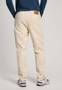 Pantalones de algodón color beige con un diseño de pierna recta, que cuentan con dos bolsillos traseros y un detalle de cuero marrón en la cintura.