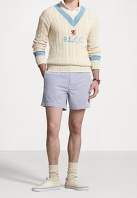 Vaaleancremistä cable-knit-neuletta sinisillä yksityiskohdilla ja brodeeratulla logolla, yhdistettynä raidallisiinShortseihin. Valkoiset lenkkarit ja beiget sukat viimeistelevät asun.