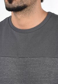 Grå T-skjorte med et strukturert stripe-design, rund hals og korte ermer. Materialet virker mykt med en glatt tekstur.