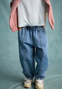 Ljusblå denim-joggingbyxor med elastisk midja och fållar, som har sidofickor och synlig sömnad. Bärs med beige sneakers.
