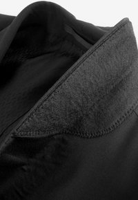Prenda negra con un suave cuello texturizado de fieltro. Presenta un forro interior suave y costuras visibles a lo largo de los bordes.
