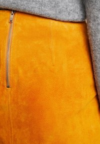 Gonna di suede gialla con una texture liscia e dettagli della zip visibili. Abbinata a un pullover grigio a maglia.