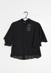 Blusa nera con colletto arricciato, tessuto trasparente, maniche corte e un design a fantasia con un piccolo dettaglio di taschino sul petto.