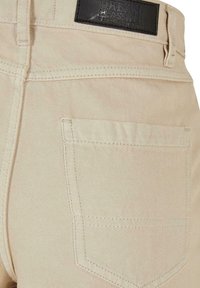 Béžové denimové kalhoty s pravou zadní kapsou s detailem šití a černou koženou etiketou na pásu.