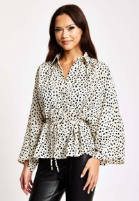 Long-sleeve blouse made of lightweight fabric, featuring a cream base with black spots, a fitted waist, and a peplum hem.