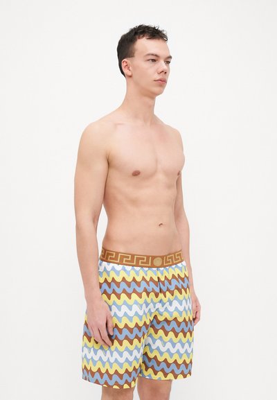 Herrarnas simshorts med ett vågigt mönster i blått, gult och brunt, med en brun midja prydd med en geometrisk design.