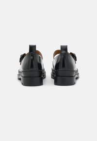 Schwarze Leder Schuhe mit glatter Oberfläche, niedrigen Blockabsätzen und dekorativen Schleifenakzenten an den Seiten. Die Rückansicht hebt die Nähdetails hervor.