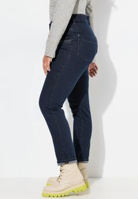 Mörkblå denimjeans med hög midja och slim fit, med bakfickor och stylade med beige stövlar med gröna sulor.