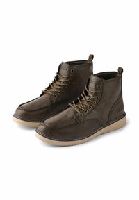 Botas de piel marrón hasta el tobillo con punta redonda, suela de goma beige, cordones oscuros y detalles de costura en la parte superior. Presenta una lengüeta.