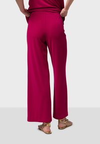 Pantalons larges fuchsia en tissu doux, avec une texture lisse et une taille élastique, associés à des sandales dorées.