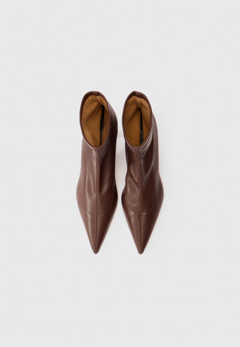 Par av bruna spetsiga ankelstövlar med en slät läderfinish och tan inredning, sedd ovanifrån på en vit bakgrund.