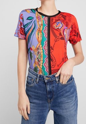 Mujer con una camiseta de manga corta y estampado colorido con diseños florales y abstractos metida dentro de unos vaqueros azules de cintura alta.