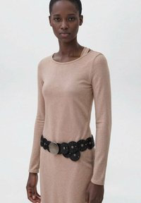 Abito a maniche lunghe di colore marrone chiaro con una cintura circolare nera dotata di dettagli metallici e ritagli posizionati in vita.