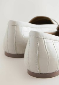 Balerini din piele albă cu model de crocodil, vârf rotunjit, toc mic și talpă exterioară contrastantă de culoare maro. Detalii cusute vizibile pe laterale.