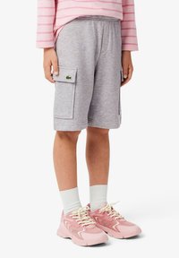 Bermuda grigie in cotone con due tasche laterali e dettaglio del logo verde. Abbinate a sneakers rosa e calze bianche. Maglietta a maniche lunghe a righe orizzontali.