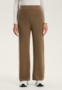 Pantaloni larghi in maglia marrone con una finitura testurizzata, vita alta e fessure laterali. Abbinati a sneakers bianche per un look informale.