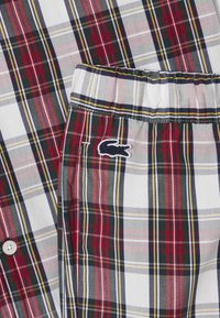 Kockás ing és sort szett, amely piros, zöld, sötétkék és sárga csíkokkal készült. Pamut anyag fehér gombokkal és hímzett logóval a sorton.