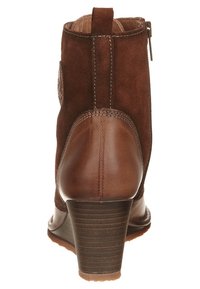 Botín de ante y cuero marrón con un tacón curvado, costuras en contraste y un parche decorativo en el lateral. Cierre con cremallera en la parte posterior.