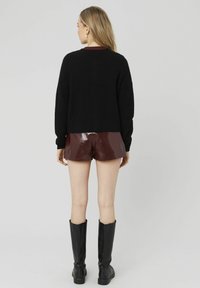 Pull noir, texture lisse, coupe cropped ; shorts bordeaux brillants ; bottes noires au genou ; arrière-plan neutre.