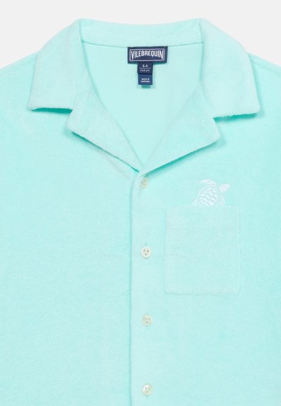 Ανοιχτό τιρκουάζ κοντομάνικο πουκάμισο με κουμπιά, γιακά, τσέπη στο στήθος και λευκό κεντημένο λογότυπο ψαριού πάνω από την τσέπη.