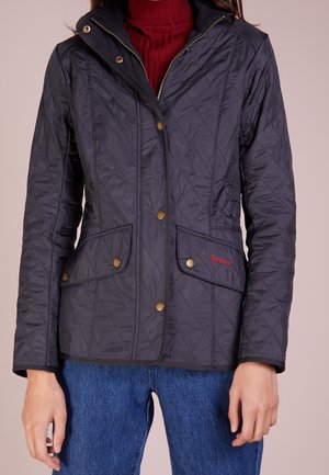 Veste matelassée marine avec quincaillerie dorée, poches avant doubles, col montant et broderie de la marque en rouge. Comprend une fermeture éclair et un tissu texturé.