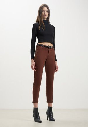 Pantaloni marroni a sigaretta con cintura, abbinati a un top nero a manica lunga. L'outfit presenta un design cropped e stivaletti neri con tacco alto e aderenti.
