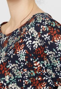 Koszulka w kwiatowy wzór na granatowym tle, z małymi czerwonymi, białymi i zielonymi liśćmi. Okrągły dekolt i miękka tekstura.