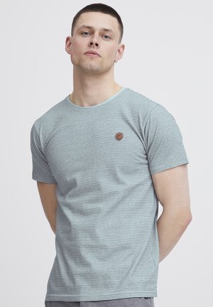 T-shirt à manches courtes rayé en teal clair et bleu marine, avec un col rond et un petit patch logo marron sur la poitrine. Tissu doux et décontracté.