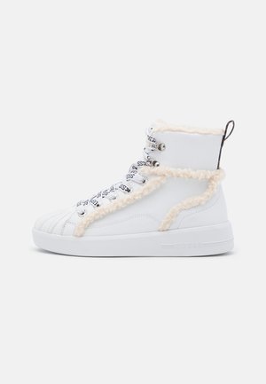 White high-top sneaker with cream faux fur trim, patterned laces, metal eyelets, thick sole, and back pull tab.