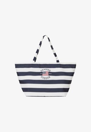 Sac fourre-tout rayé bleu marine et blanc avec poignées, avec le texte « Seaside Oregon » et un petit drapeau américain avec des coordonnées au centre devant.